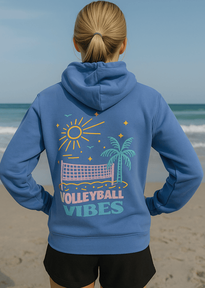 Person wearing a blue hoodie with 'Volleyball Vibes' design on a beach